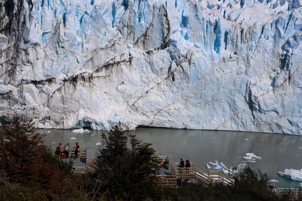 A metal pathway with a few tourists on it sits in front of a glacier in Patagonia