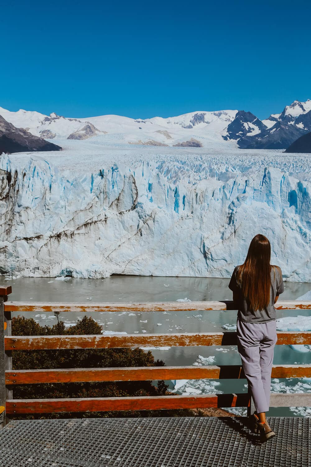 A woman stands at a viewing deck against a handrail looking at a glacier