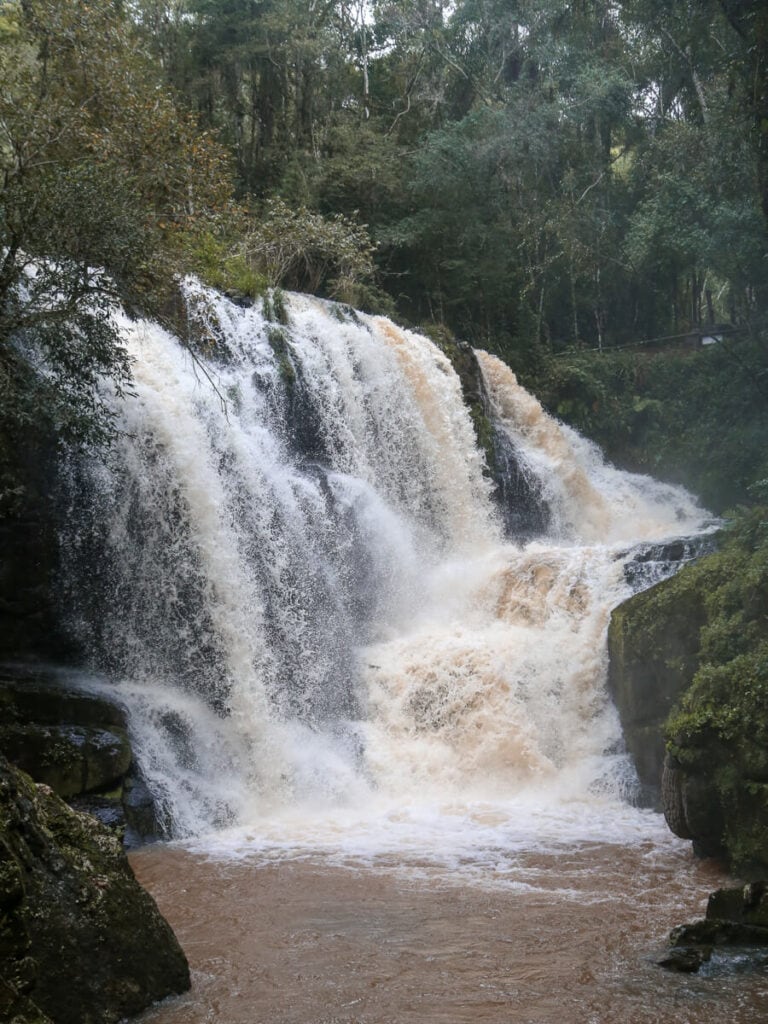 A gushing brown waterfall pours down into a river in the jungle