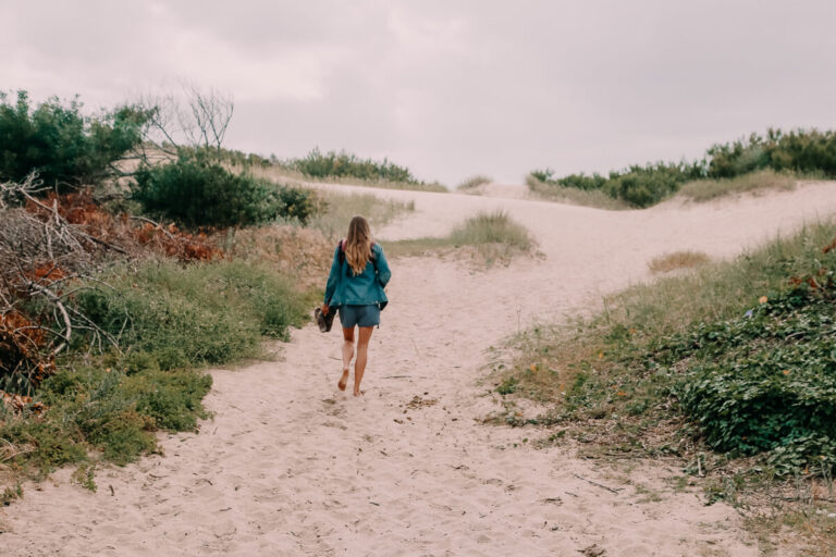 A woman walks up a sand dune carrying her flip flops in her hand