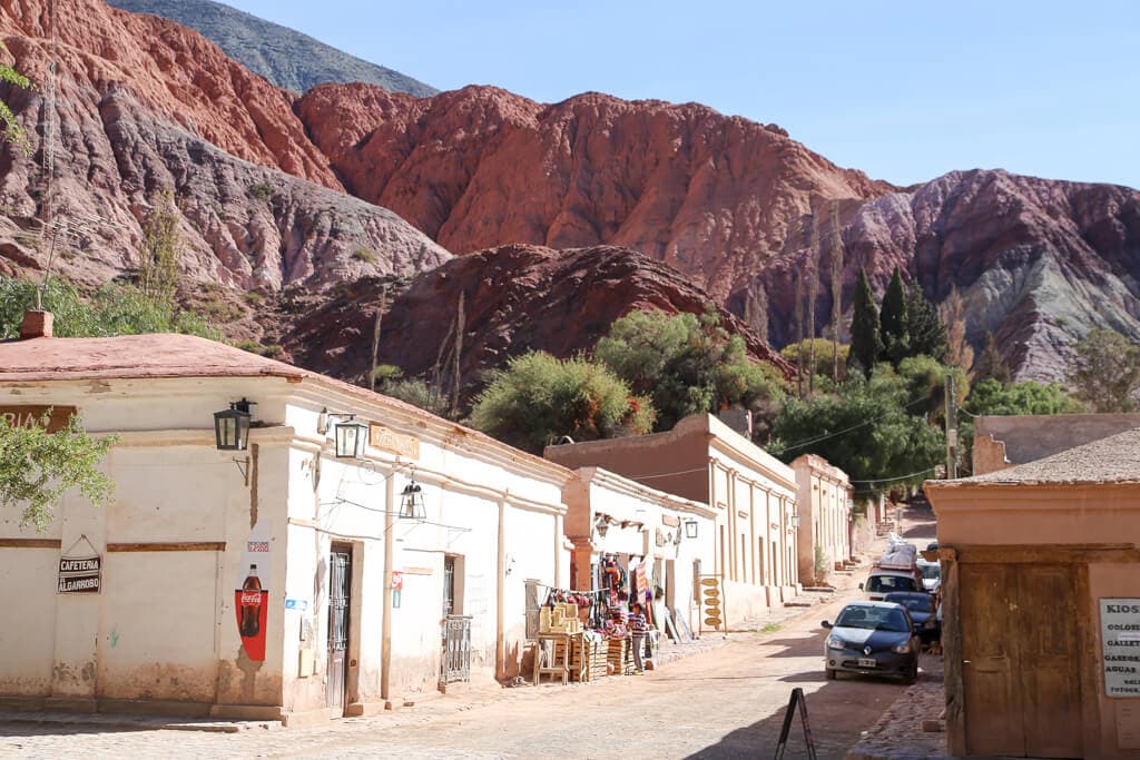 Adobe one story buildings go uphill in front of red mountains