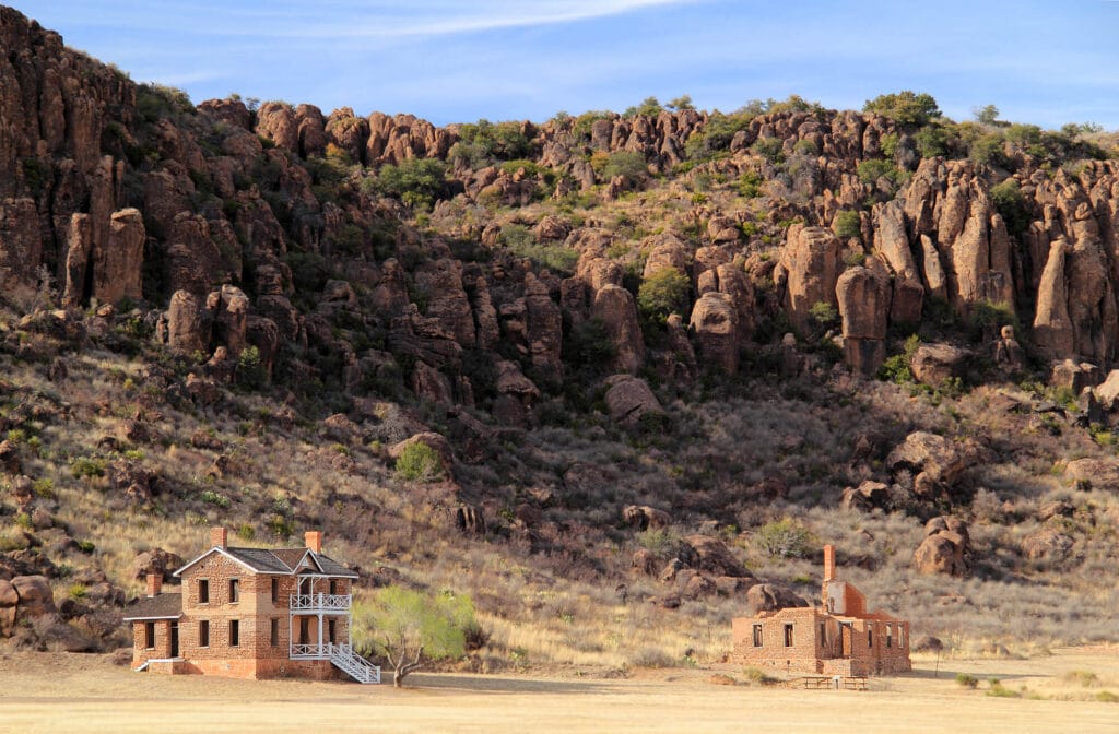 Two brick buildings in a desert with rocky mountains rising up behind them