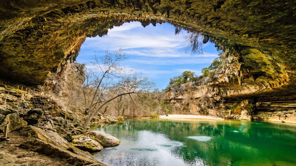 A turquoise blue swimming hole with a rocky cliff over it