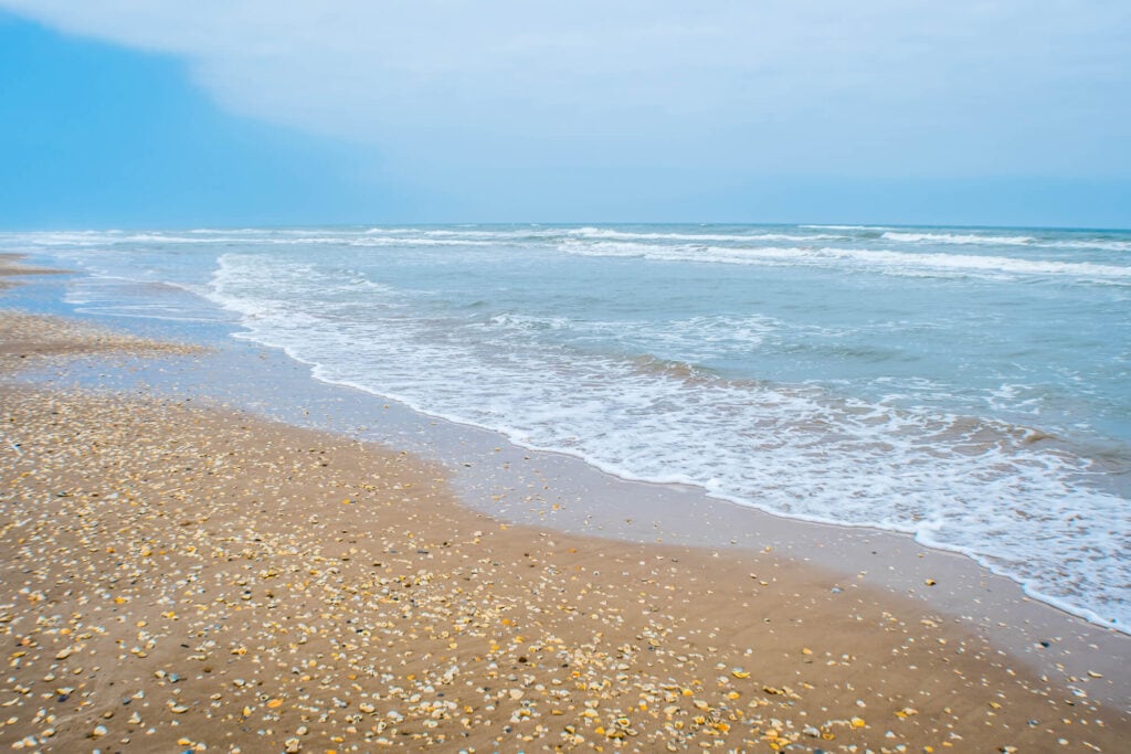 The ocean waves wash up on a seashell covered beach