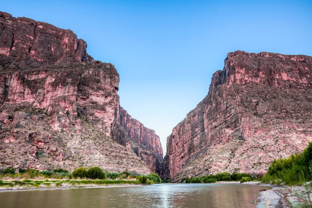 Bright red cliffs frame a canyon with a river flowing through it