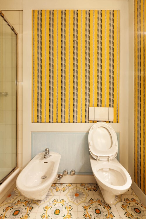 A toilet and a bidet in a bathroom with yellow wallpaper