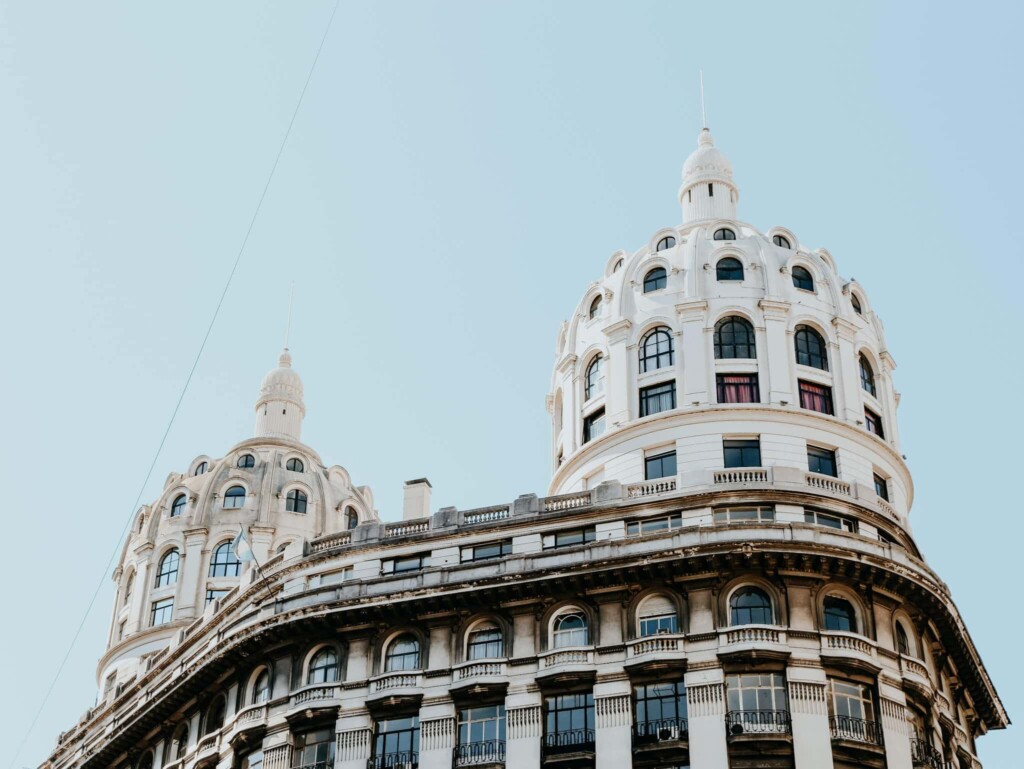 A white building with two round domes towers over a pale blue sky