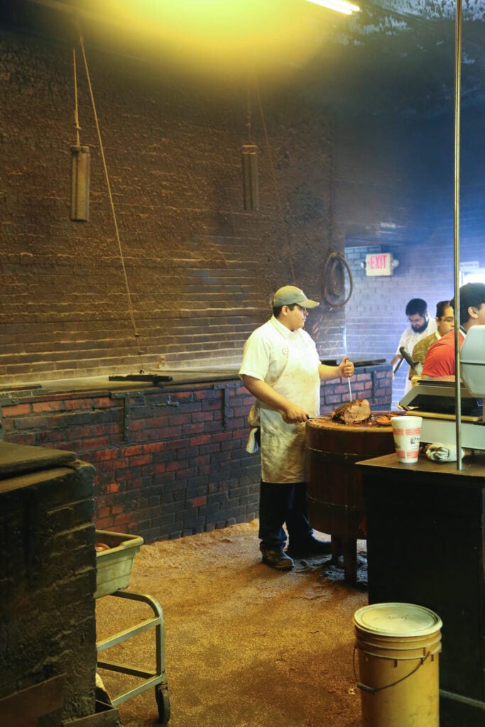 A man in a white apron carves a brisket on a butcher block