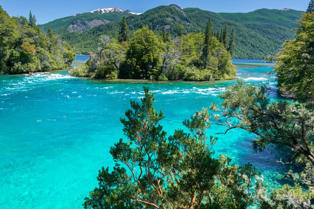 Crystal clear turquoise water in a lake surrounded by bright green trees