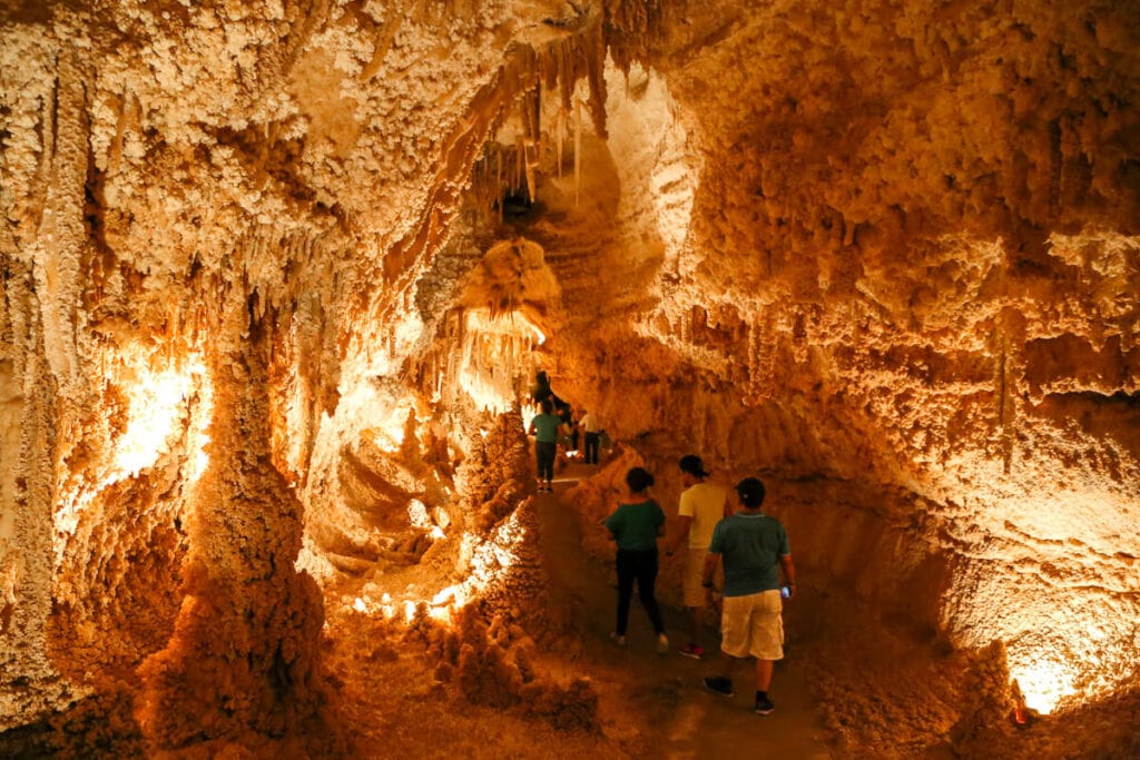 A line of people walk on a path in a cave under countless formations hanging overhead