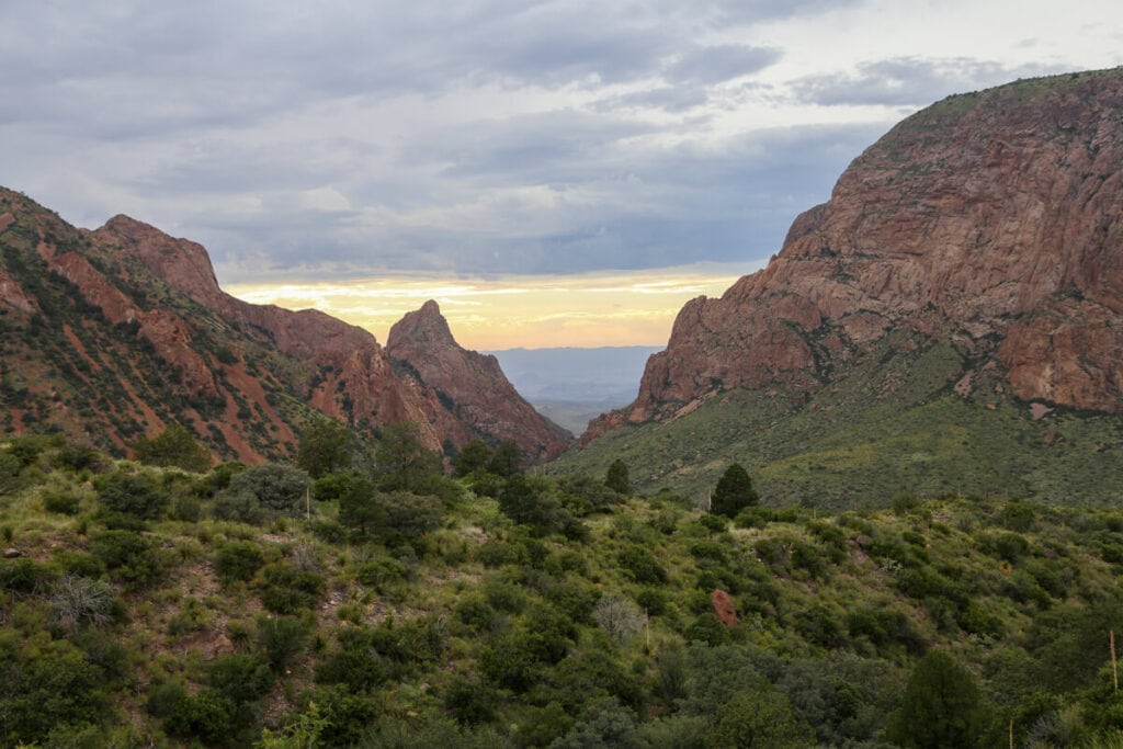 The sunset and a yellow sky tower over red mountains and a green canyon