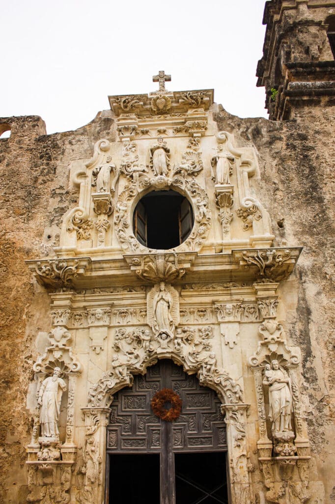 The front facade of a catholic church in a historic mission with a cross on top and statues decorating the facade