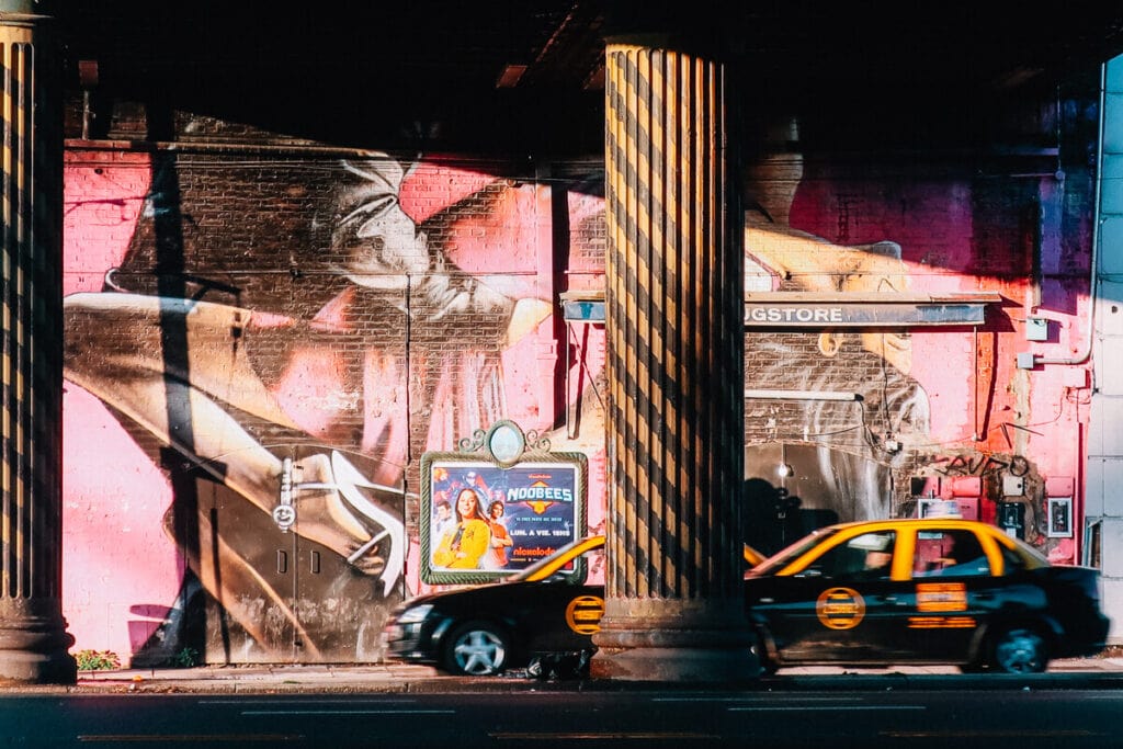 A pink mural of two tango dancers by a road with two taxi cabs driving past