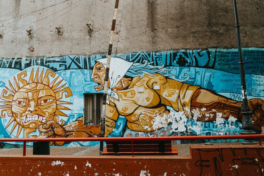 A mural of a woman in a white bandana and yellow shirt with her hand in a fist by a sun