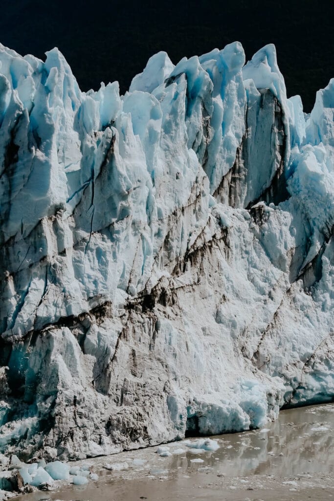 A wall of turquoise blue ice covered with dirt.