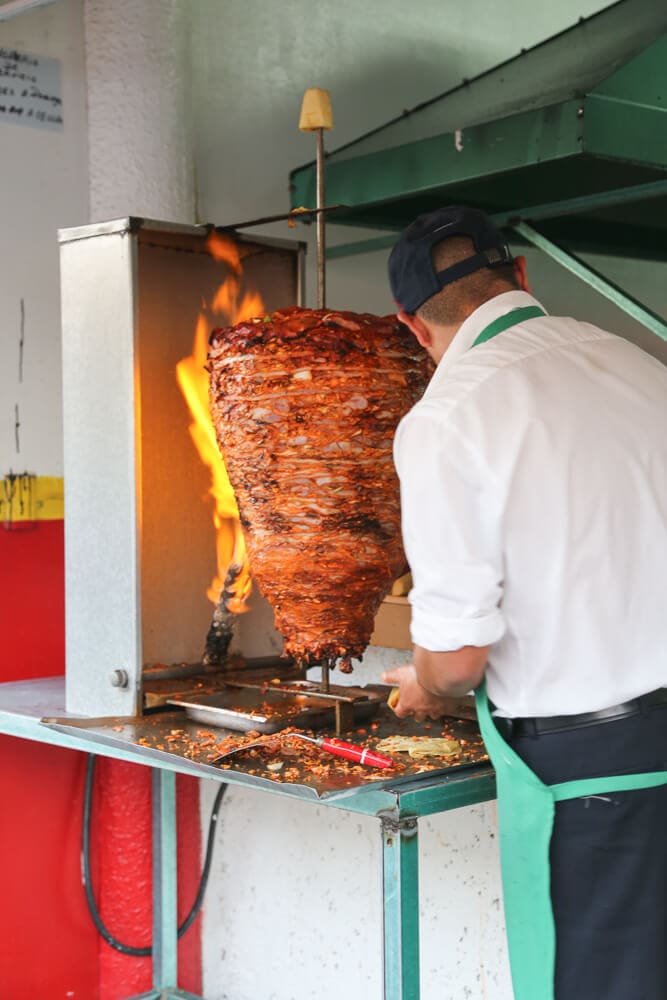 A man cuts meet off a trompo of meat at a taqueria