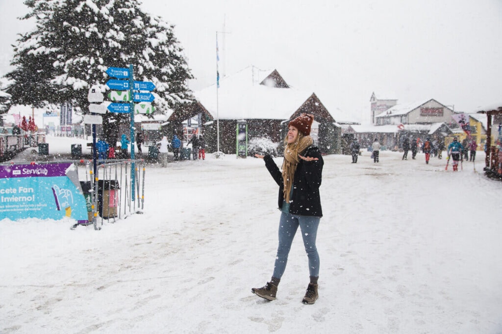 A woman stands in the snow with her hands up catching snowflakes