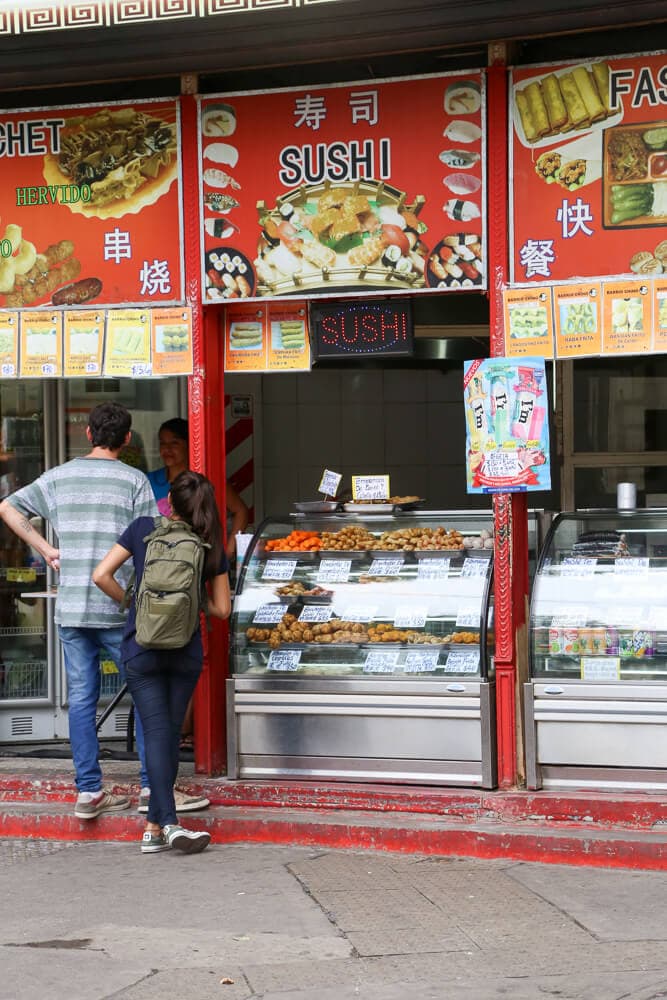 Two people stand at an outdoor food counter selling sushi