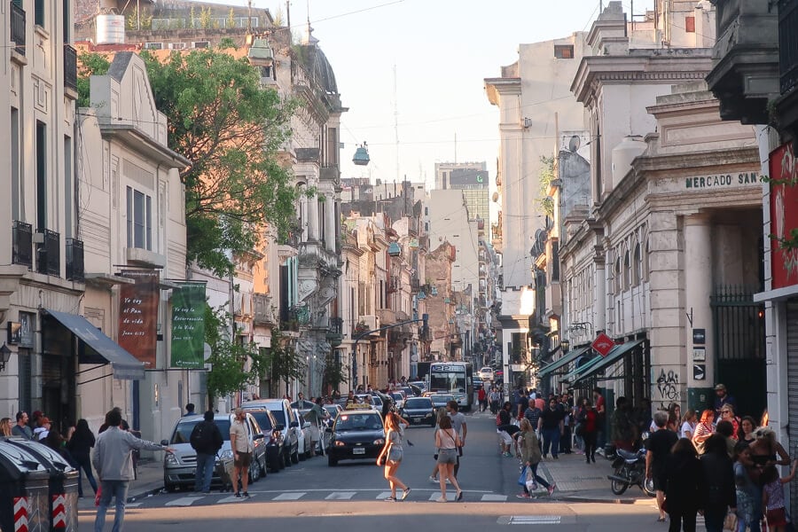 People cross the street in San Telmo in front of taxis and buses