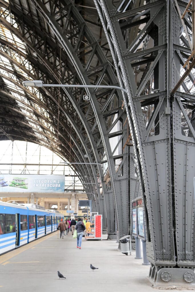 Metal arches rise over the train platform next to a blue train