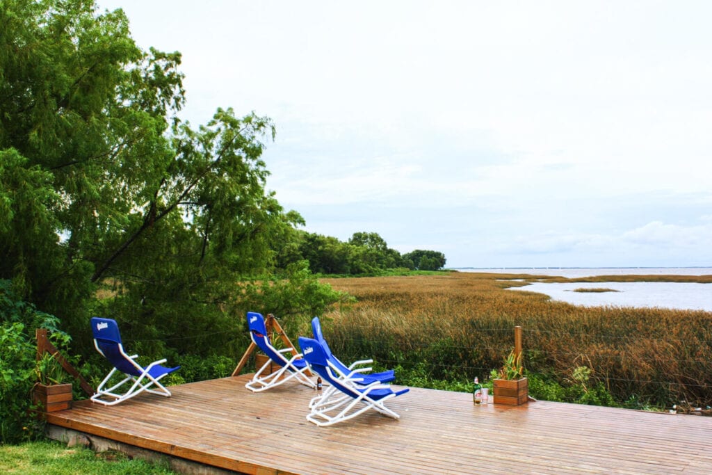 Four blue lawn chairs on a deck by a river