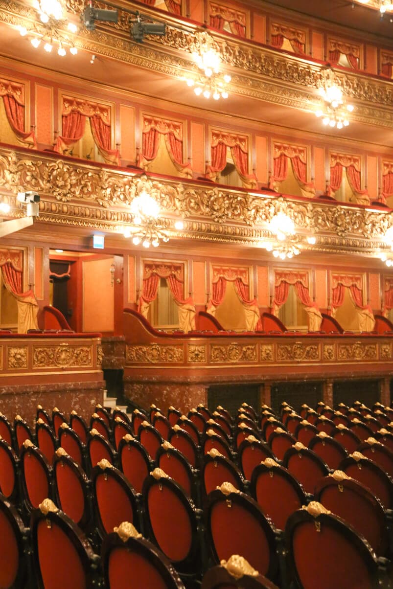 An opera house with red and gold seats and golden detailed balcony seating