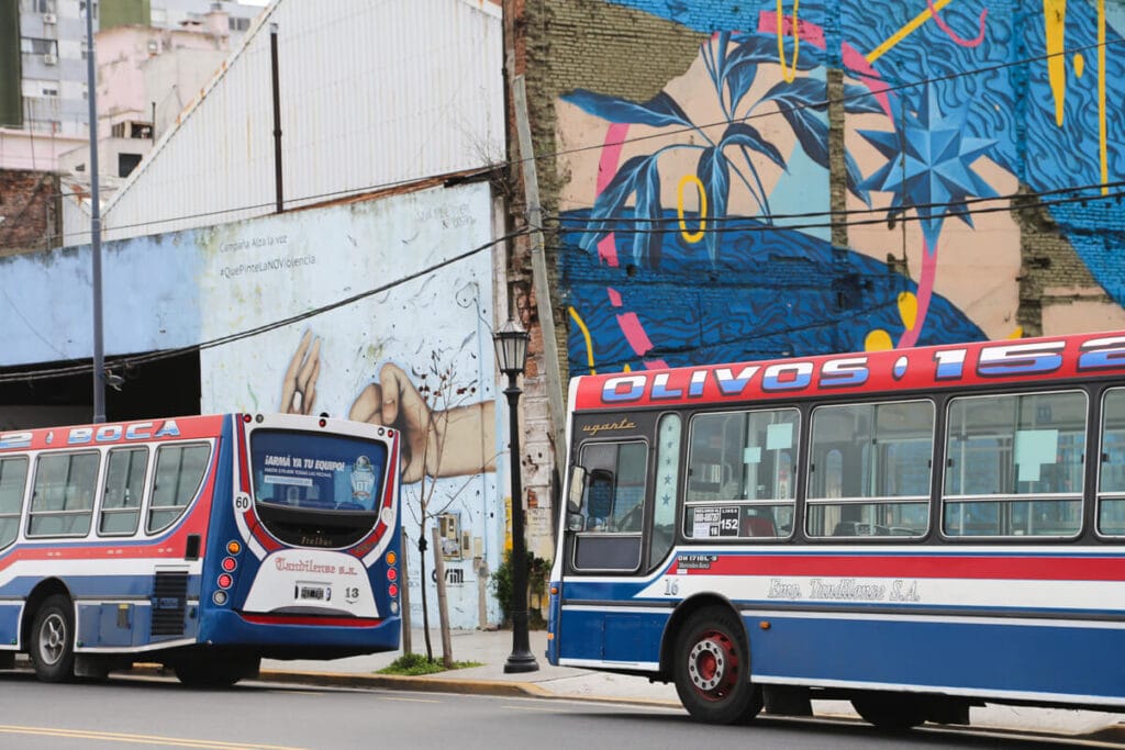 Two buses parked next to a mural