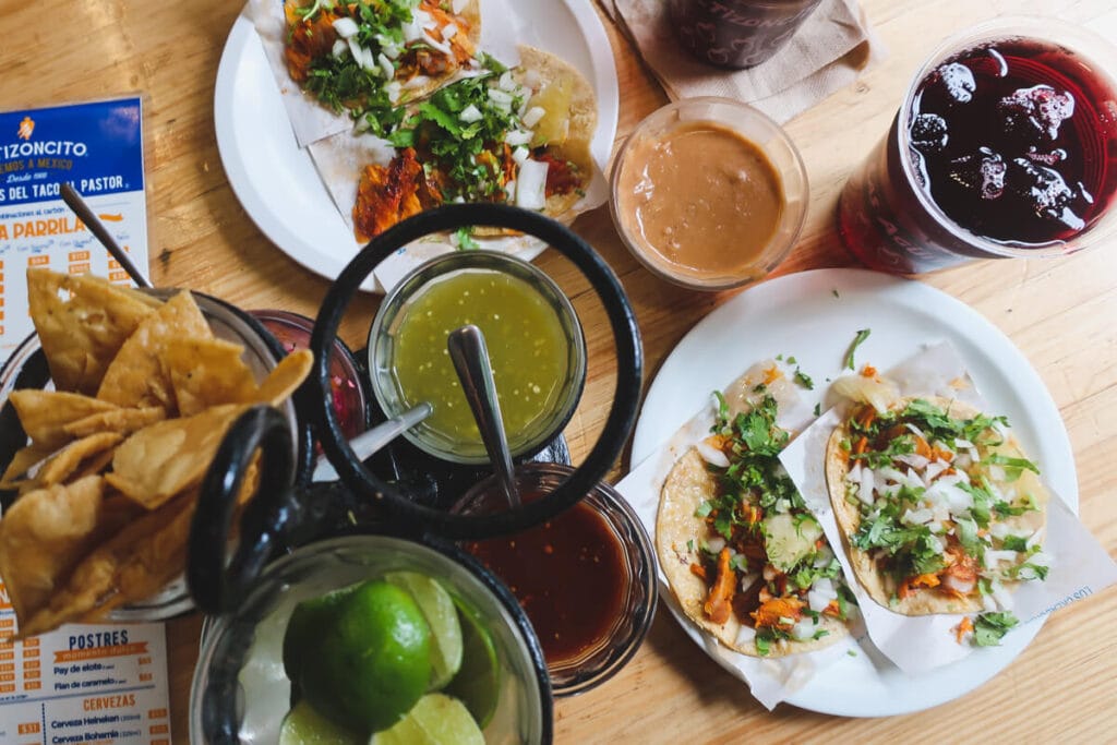 Two plates of tacos surrounded by chips and dips on a wooden table