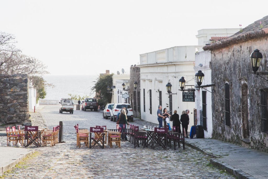 Tables and chairs on a cobblestone street next to colonial buildings