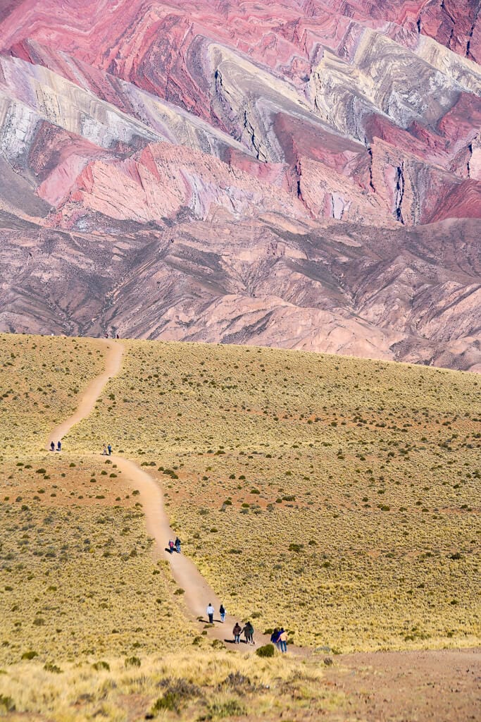 A dirt path winds down a desert landscape towards a red mountain