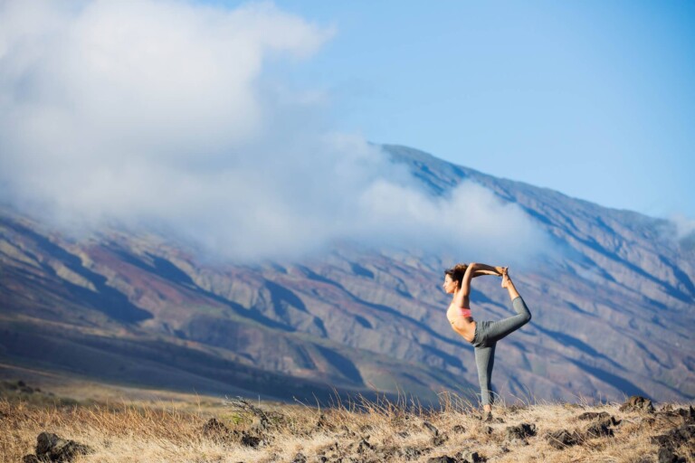 A woman does dancer pose doing yoga in the mountains