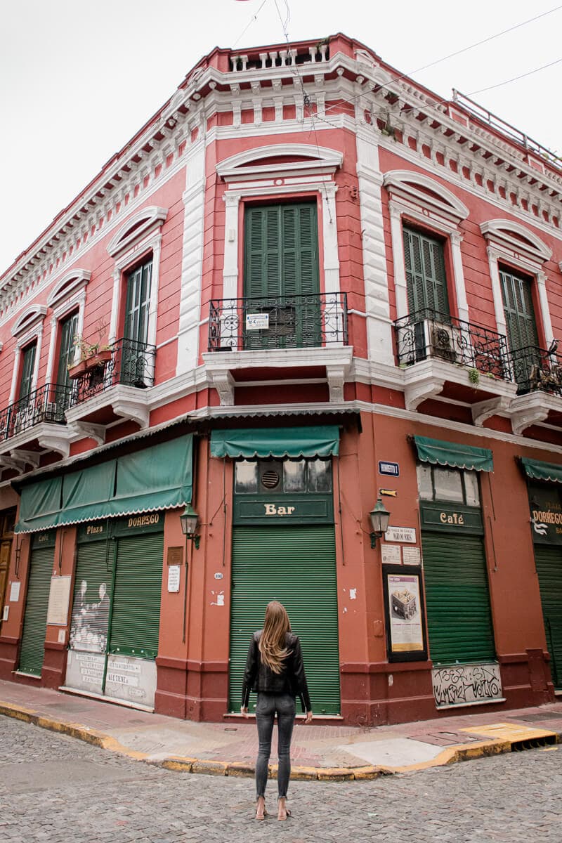 A woman in black stands with her back to the camera looking a red building