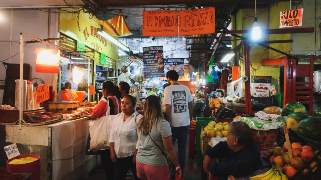 A woman walks through a busy hall down a Mexico City market b fruit and taco vendors