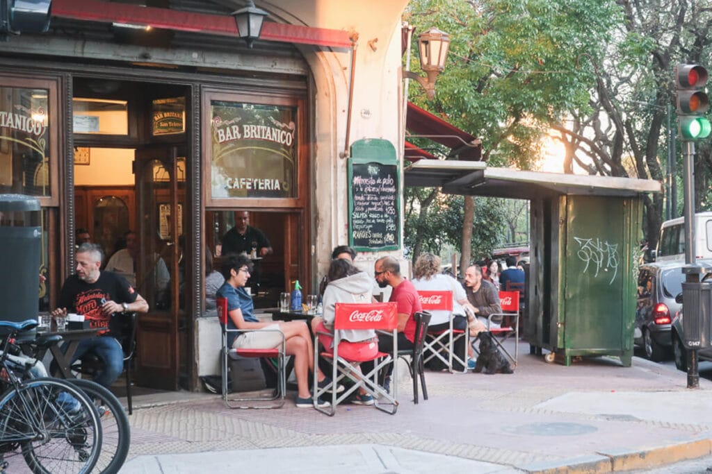 People sit at a sidewalk cafe in front of an old Argentine bar on a street corner