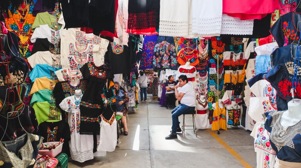 A rainbow of colorfully embroidered blouses hang in a market in Mexico City