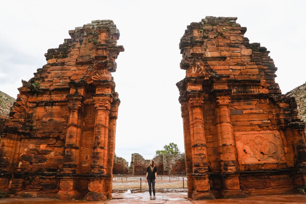 A woman in black stands between two doors in the ruins of a Jesuit Mission