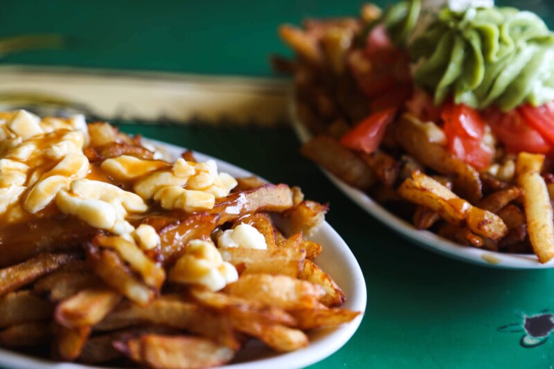 Two plates of french fries with cheese and tomato toppings