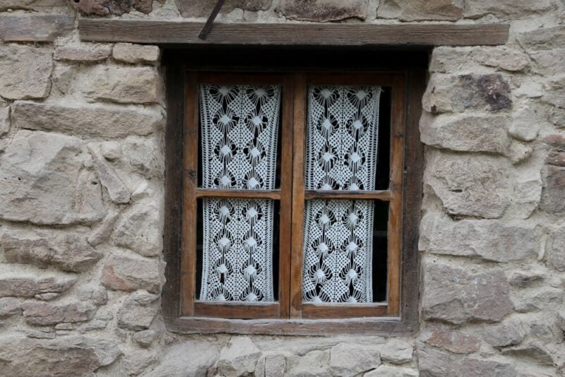 A lace curtain in a wooden window frame in a stone wall