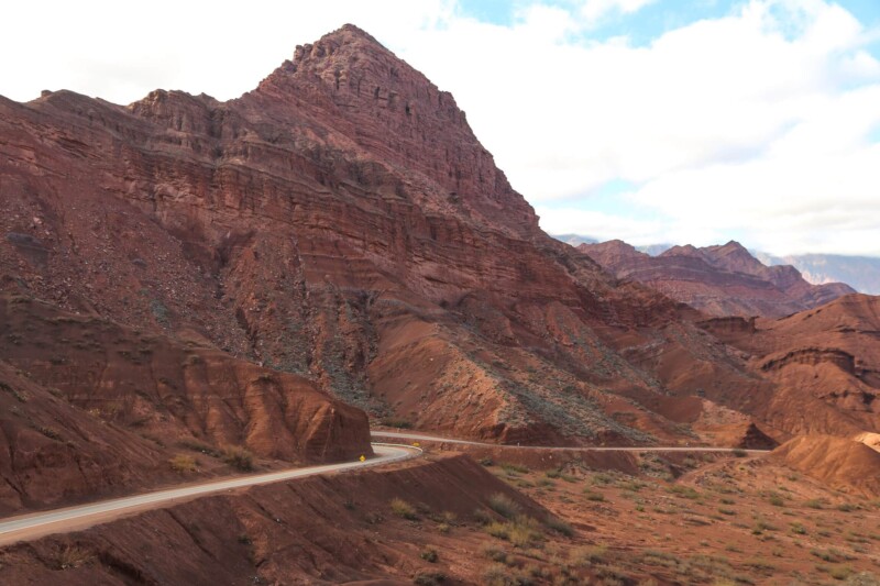 A highway in the desert clings to a red mountain