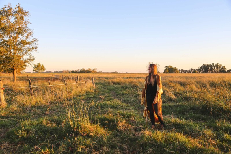 A woman stands in a pasture at sunset