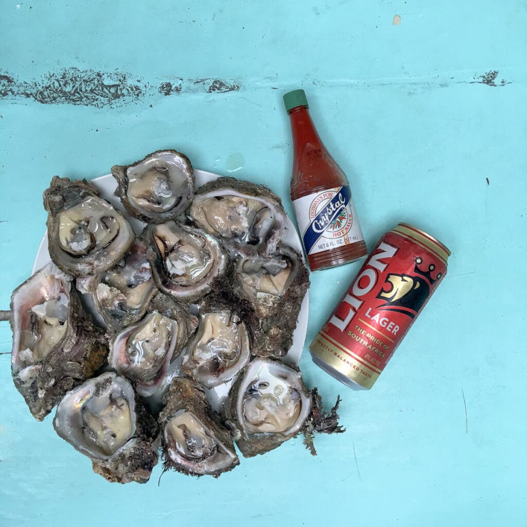 A plate of oysters next to a bottle of hot sauce and a can of beer