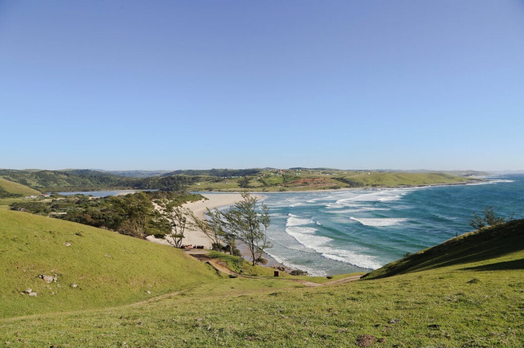 Ocean waves wash up to the beach at the foot of large hills