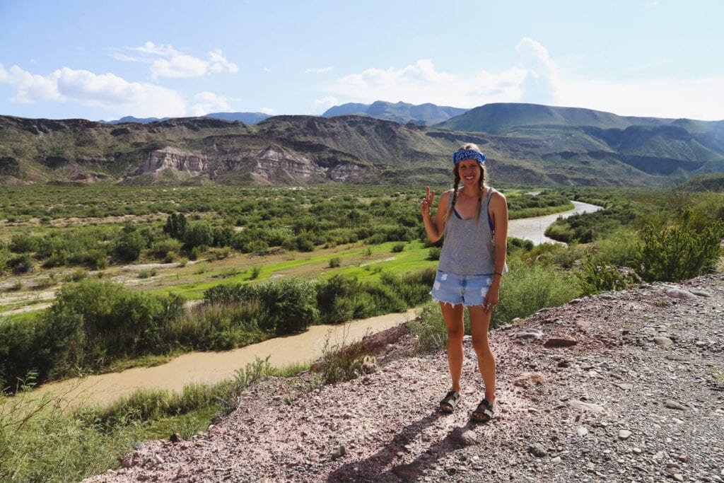 A woman does the peace sign by a river in the desert