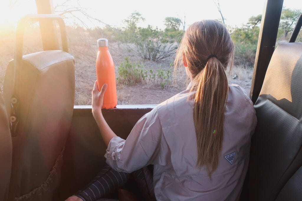 A woman sits in a truck with an orange water bottle in her hand on a South Africa safari