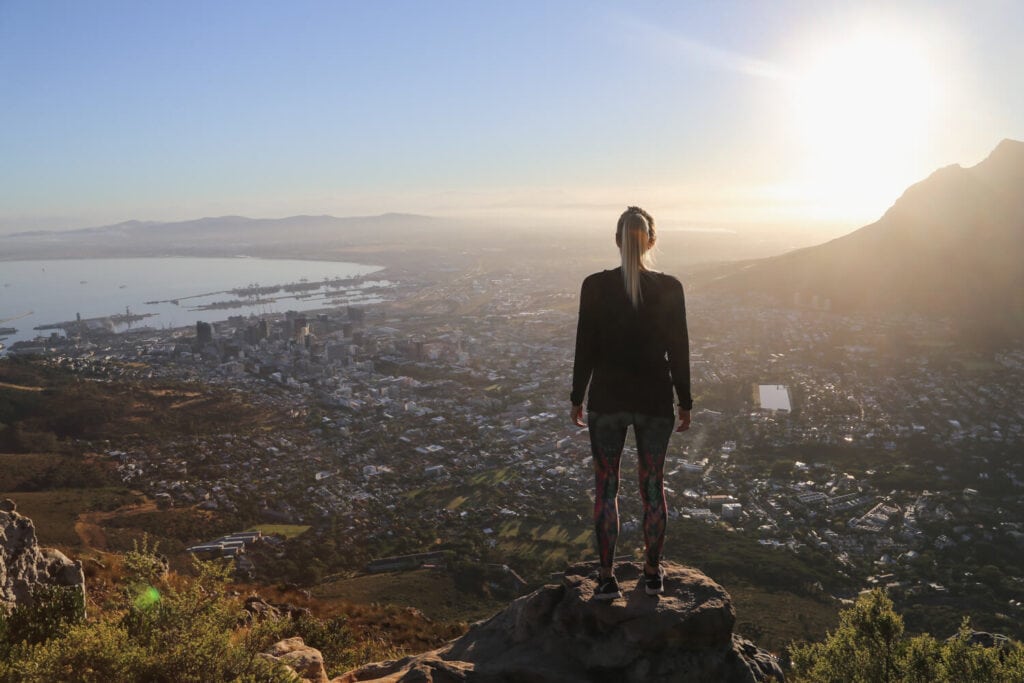 A woman stands on a rock on a cliff overlooking a city below