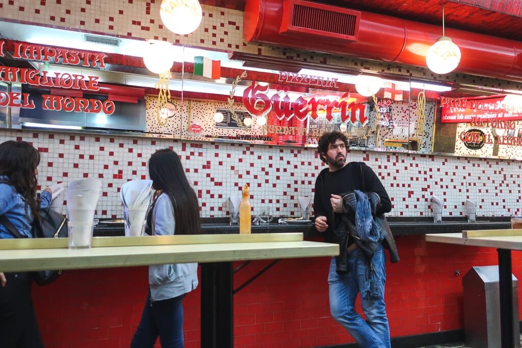 A man leans against a bar in a red and white tiled restaurant