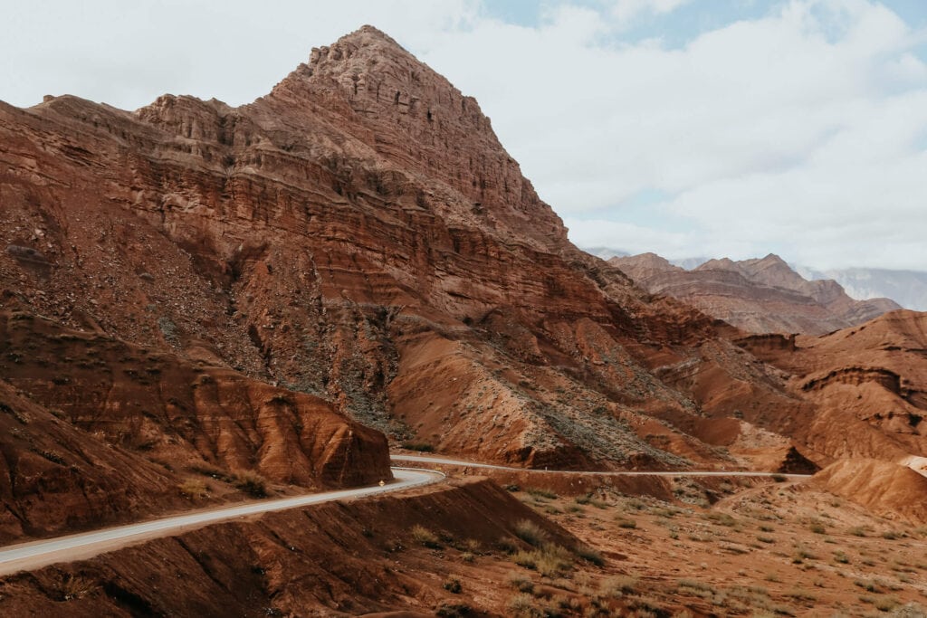 A highway weaves along next to a red mountain in the desert