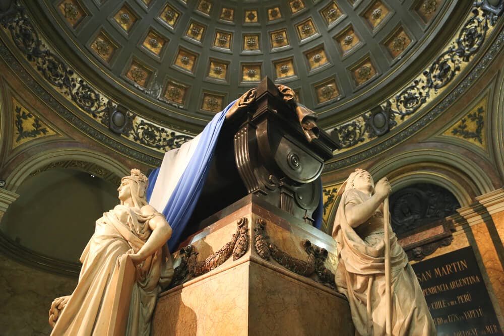 A mauseleum seen from below with a blue and white flag draped over it