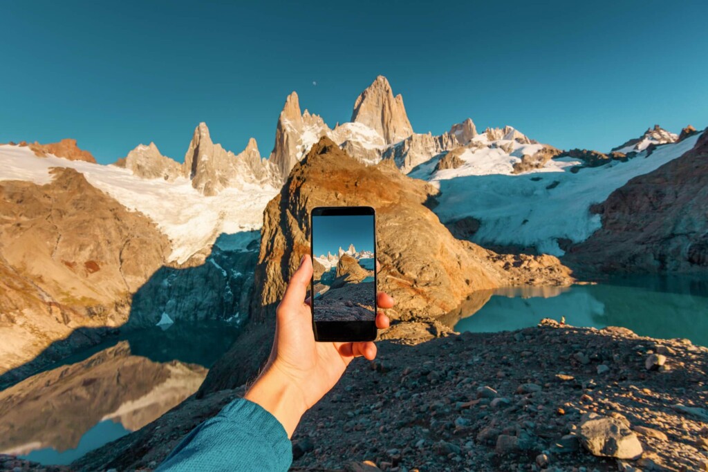 A hand holds a phone out in front of them in front of the mountains in Patagonia