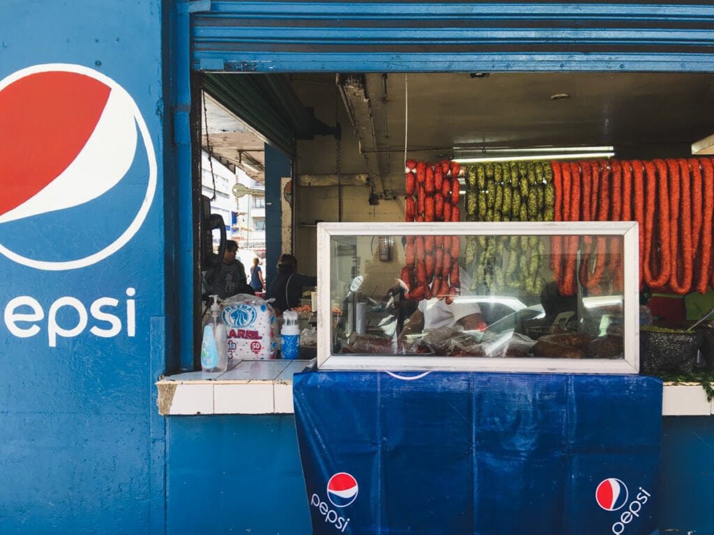 Links of red and green sausage hang in a window by a blue wall